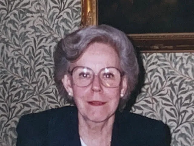 Sylvia Bacon in later life: grey hair, wire-rimmed glasses, a dark jacket.